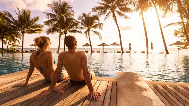 Booking a foreign holiday couple sat by pool sunset